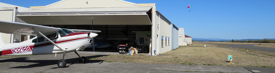 A small aircraft is parked in front of a hangar at the airport.